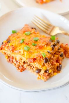 a white plate topped with lasagna covered in cheese and black beans next to a fork