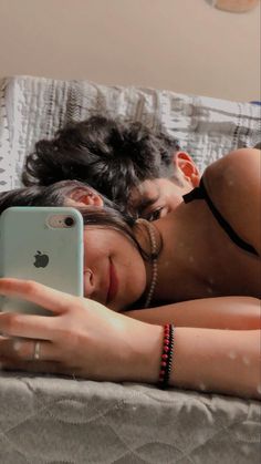 a woman laying on top of a bed next to a man holding an apple phone