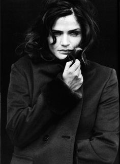 a black and white photo of a woman holding something in her hand while wearing a coat