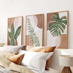 three paintings on the wall above a bed with white linens and gold pillow cases