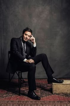 a man in a suit and tie sitting on a chair talking on a cell phone