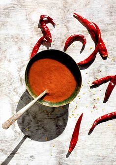 a bowl filled with red hot sauce next to some chili peppers