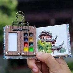 a person holding up a miniature book with some art supplies in it's pages