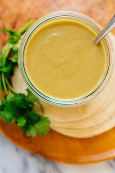 a glass jar filled with yellow liquid sitting on top of a wooden plate next to cilantro