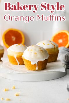 three orange muffins on a plate with icing and an orange in the background