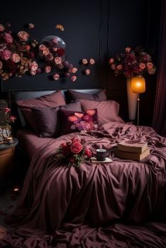 a bed covered in purple sheets and pillows next to a table with flowers on it