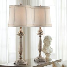 two lamps sitting on top of a table next to a white busturine and lamp shade