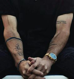 a man with tattoos on his arm sitting down and holding his hands in front of him