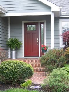 a red front door on a gray house with brick steps and plants in the foreground