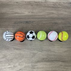 five different colored balls lined up in a row on a wooden surface, one with a soccer ball and the other with a basketball