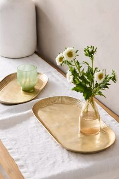 two gold plates with flowers in them sitting on a white table cloth next to a vase