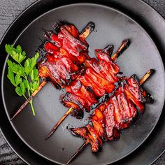 a plate with some meat on skewers next to a green leafy garnish