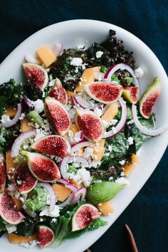 a salad with figs, onions and cheese on it in a white bowl next to utensils