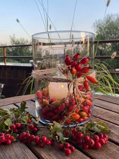 a glass vase filled with berries and a lit candle on top of a wooden table