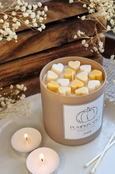 some candles are sitting on a table next to flowers and a box with marshmallows in it