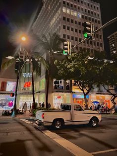 a white truck driving down a street next to tall buildings and traffic lights at night