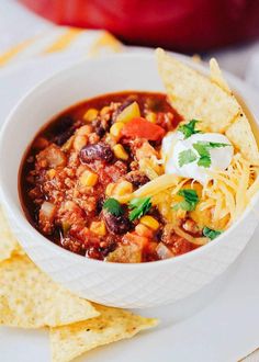 a white bowl filled with chili and tortilla chips on top of a plate