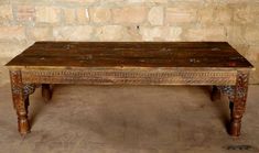 an old wooden table sitting in front of a brick wall with no one around it