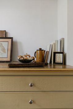 an old dresser with books and pictures on it's top, along with a bowl of mushrooms