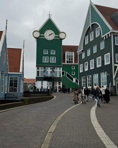 several people walking down a cobblestone street in front of buildings with clocks on them