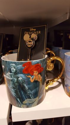 the little mermaid mug is on display in front of other disney character coffee mugs