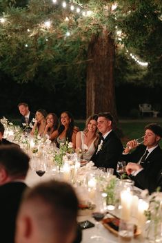 a group of people sitting at a dinner table with candles and wine glasses in front of them