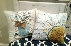 two decorative pillows with daisies in a mason jar on a blue and white bench