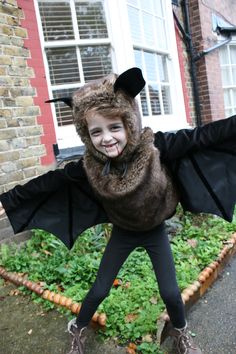 a young boy dressed as a bat standing in front of a brick building with his arms outstretched