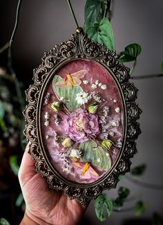 a close up of a person's hand holding an ornate frame with flowers on it