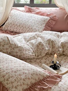 a candle is lit on a bed with pink comforters and pillows in front of a window