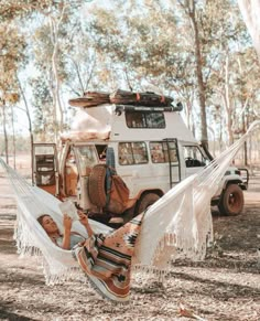 two people laying in a hammock on the ground next to a van and trees