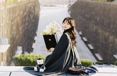 a woman sitting on the ground holding a book with flowers in her lap and a stuffed animal next to her