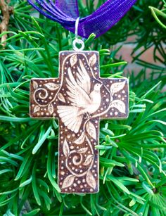 a cross ornament hanging from a tree with purple ribbon in the foreground