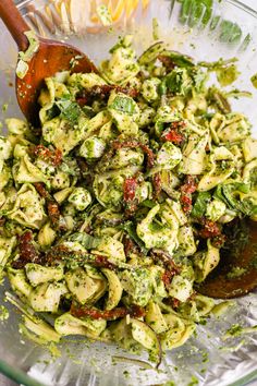 a glass bowl filled with pasta and pesto sauce next to a wooden spoon on top of a table