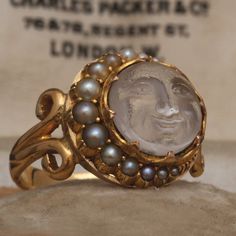 This sweet, spectacular, and collectible Victorian era man in the moon ring is a rare find. Most likely converted from a brooch in the late 19th century, the head features a sculpted glass cabochon representing the kindly visage of the man in the moon. The celestial center stone is partially framed by a crescent of seed pearls and sits within low scalloped prongs. The handwrought 18k yellow gold mounting features elegantly bifurcated shoulders and a half round hoop. Antique Collectible Moonstone Ring, The Man In The Moon, Moon Jewellery, Victorian Man, Man In The Moon, In The Moon, Moon Ring, Dope Jewelry, Funky Jewelry