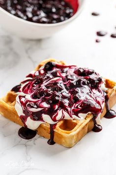 a waffle topped with blueberry sauce and whipped cream next to a bowl of berries