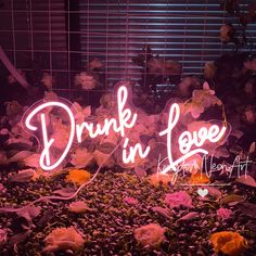 a pink neon sign that says drunk in love with flowers on the ground next to it