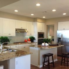 a large kitchen with white cabinets and granite counter tops, an island in between two bar stools