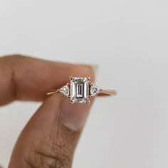 a woman's hand holding an emerald and diamond engagement ring in front of her face