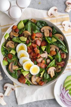 a bowl filled with spinach, mushrooms and hard boiled eggs on top of a table