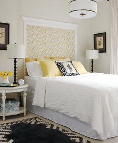 a white bed with yellow and black pillows in a bedroom next to a lamp on a table