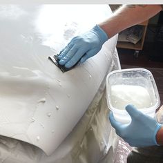 a person in blue gloves is painting a white car with foam on the hood and another hand holding a brush