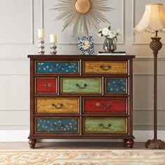 a multicolored chest of drawers sitting on top of a rug next to a lamp