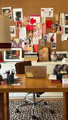 a desk with a laptop computer on top of it next to a wall covered in pictures