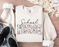 a white sweatshirt with the words school nurse on it next to some shoes and blankets