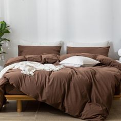 an unmade bed with brown sheets and white pillows on top of it next to a potted plant