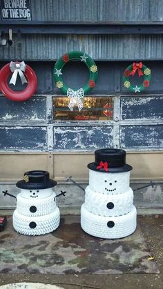 two snowmen sitting on the ground in front of a building with christmas wreaths