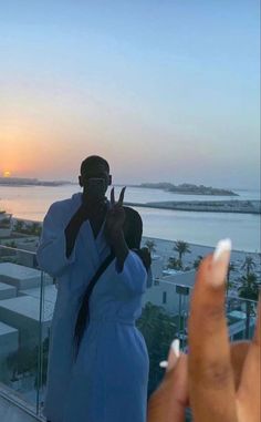 two people taking pictures with their cell phones in front of an ocean view at sunset