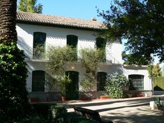 a large white house sitting next to a lush green tree covered park area on a sunny day