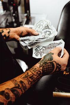 a man with tattoos on his arm holding up some paper in front of the camera